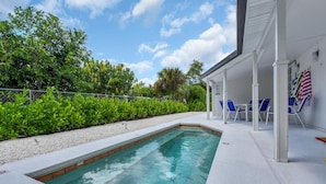 A rectangular swimming pool with a white deck, surrounded by lush greenery and a covered seating area with blue chairs. - Holiday Lane - Discover the ultimate vacation retreat at Holiday Lane! (Naples)