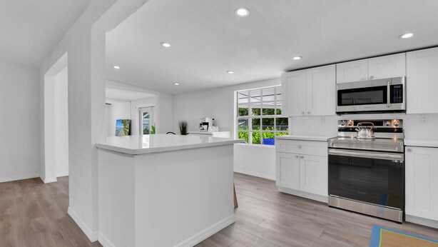 A modern kitchen with white cabinetry, stainless steel appliances, and a large window providing a view of greenery outside. - Holiday Lane - Discover the ultimate vacation retreat at Holiday Lane! (Naples)