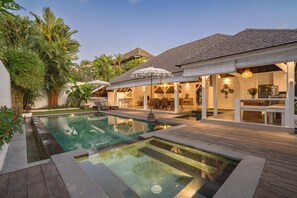 Een zwembadgedeelte met een jacuzzi, een houten terras en buitenmeubels.