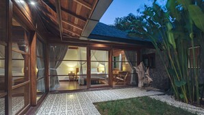 A modern hotel room with large glass doors, a bed, and a sitting area with a view of the garden. - Villa Lou Ann (Canggu)