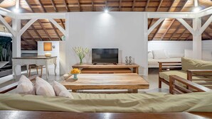 A spacious living area with a high ceiling, wooden beams, a central table, a sofa, and a television. - Villa Lou Ann (Canggu)
