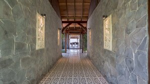 A stone-walled corridor with patterned flooring, leading to a covered area with tables and chairs. - Villa Lou Ann (Canggu)