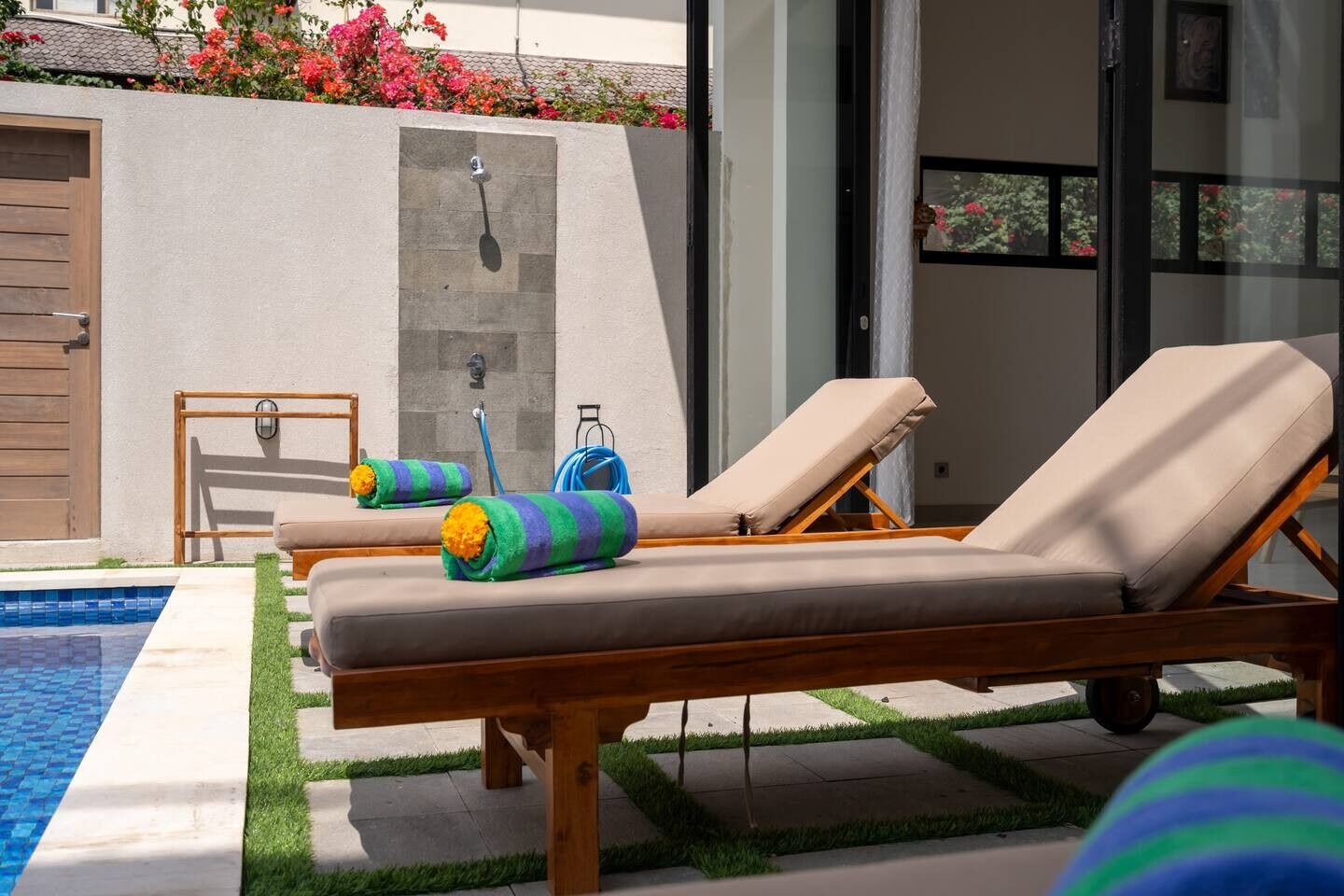 A poolside area with two lounge chairs, a wooden bench, and a hose.