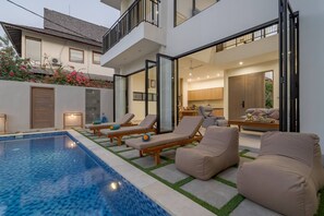 Ein modernes Haus mit Swimmingpool, Sitzgelegenheiten im Freien und einem gut beleuchteten Innenraum.