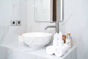 Une salle de bain avec un lavabo en marbre blanc, un miroir, un distributeur de serviettes et une bouteille de shampoing.