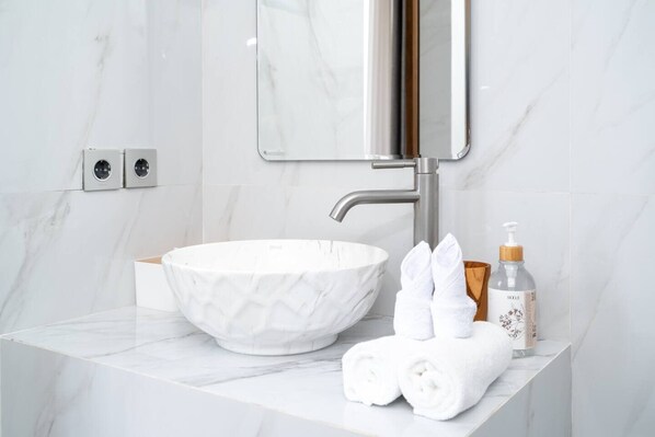 A bathroom with a white marble sink, a mirror, a towel dispenser, and a bottle of shampoo. - Zen Villa - Central Canggu (Canggu)