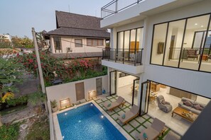 Une maison moderne à deux étages dotée d’une piscine, d’un espace salon extérieur et d’un balcon.