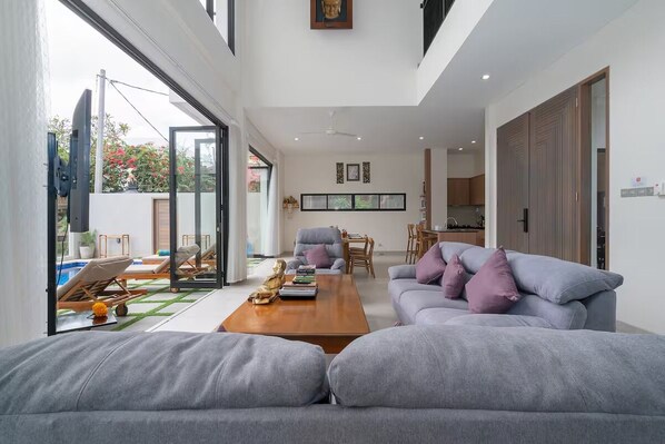 A modern living room with a grey sofa, a wooden coffee table, and a dining area in the background. - Zen Villa - Central Canggu (Canggu)