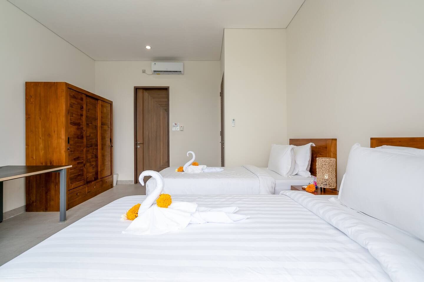 A hotel room with two beds, wooden wardrobe, and a small table.