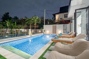 Ein moderner Poolbereich im Freien mit Liegestühlen und einer verglasten Terrasse.