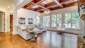 Un salon spacieux doté de planchers en bois franc, d’un canapé d’angle, d’un fauteuil blanc et de grandes fenêtres offrant une vue sur l’extérieur.