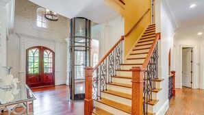 Un intérieur spacieux agrémenté d’un escalier en bois, d’un ascenseur en verre et d’une grande porte cintrée.