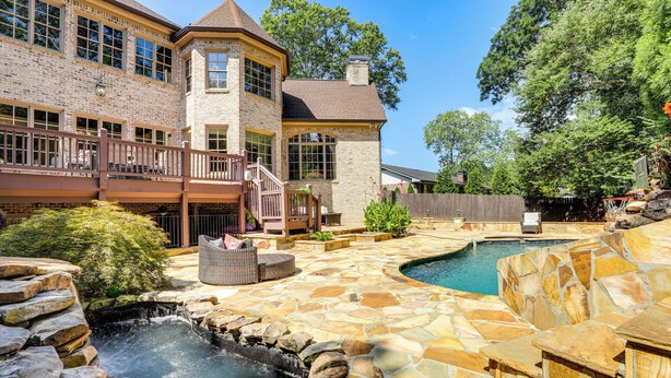 Une terrasse en pierre avec une piscine, une cascade et une maison à plusieurs niveaux dotée d’un balcon.