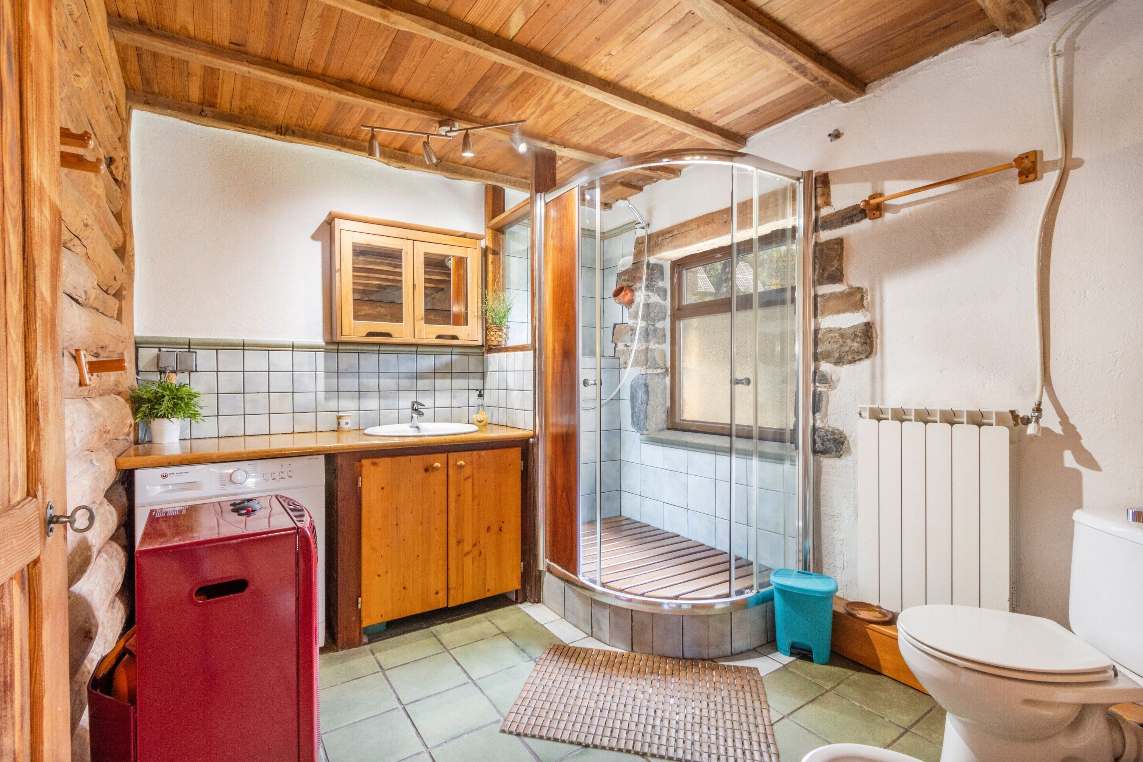 A bathroom with a wooden ceiling, a glass shower enclosure, a sink, and a toilet.