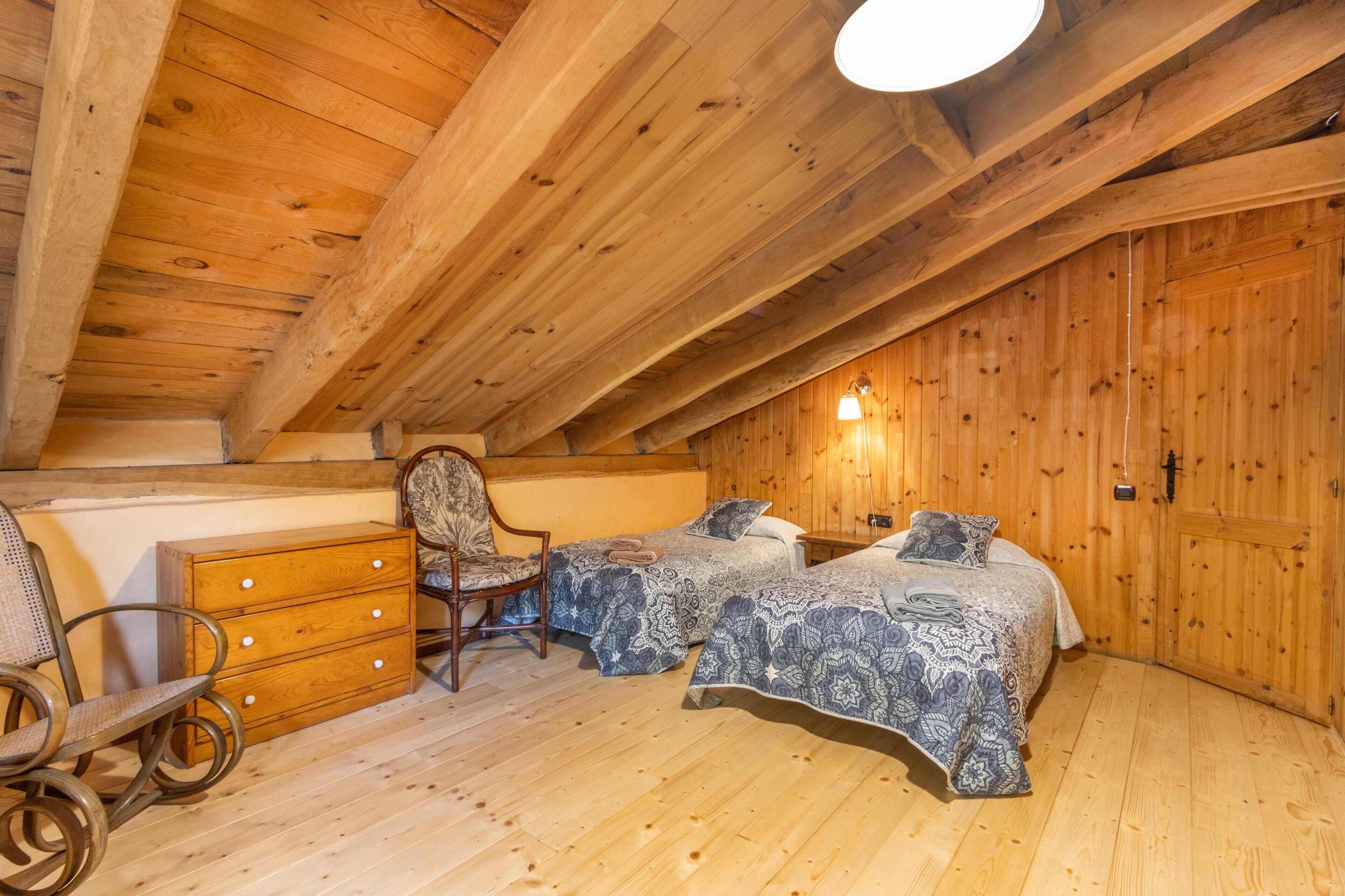 A wooden room with two beds, a dresser, a chair, and a ceiling light.