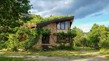Una casa de piedra con techo inclinado, muros cubiertos de hiedra y un banco al frente.
