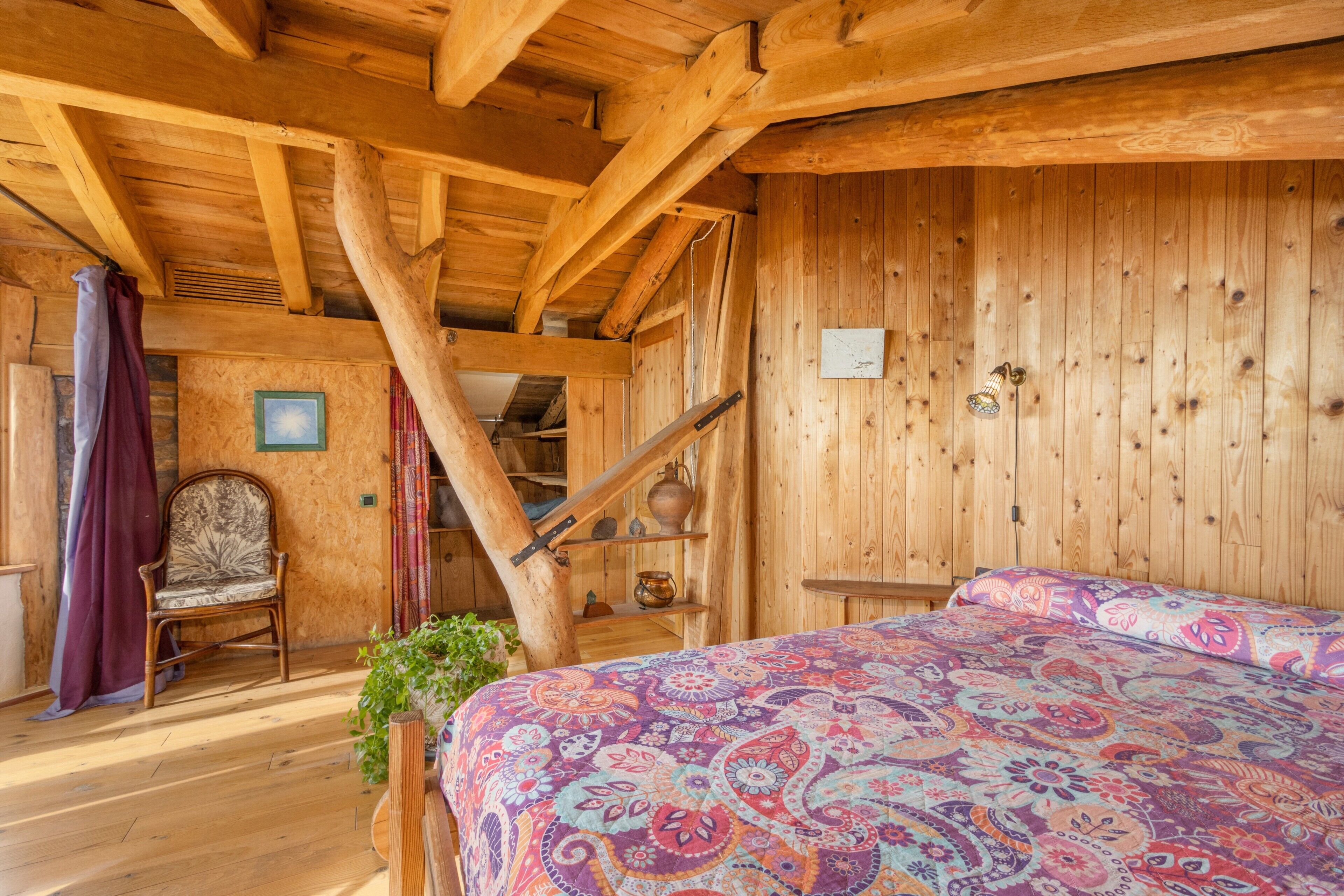 Interior de una cabaña de madera con una cama, una silla y una escalera.