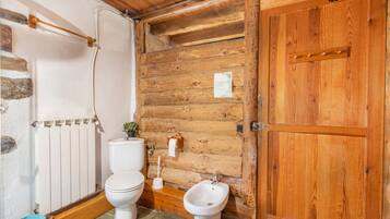 A wooden cabin bathroom with a toilet, bidet, and wooden walls.