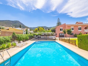 Une piscine agrémentée d’une pergola et de chaises longues, entourée de verdure et avec une chaîne de montagnes en toile de fond.
