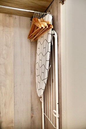 A room with a wooden floor, a metal rack with hangers, and a white curtain with a geometric pattern.