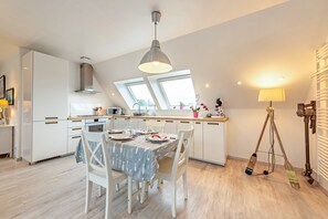 A modern kitchen with white cabinetry, a dining table with a patterned tablecloth, and a ceiling light fixture. - Apartment 'Plougasnou Proche Mer' with Wi-Fi (Plougasnou)