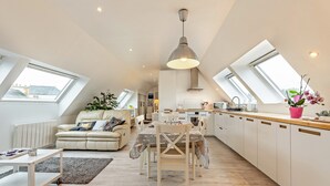 A modern loft apartment with a dining area, kitchen, and living space, featuring skylights and a large pendant light.