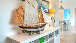 A model ship on a white shelf, a framed picture on the wall, and a lamp in the background.