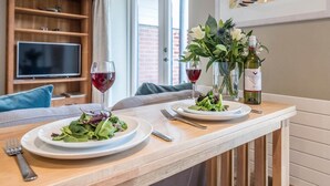A dining table with two plates of salad and two glasses of red wine, a bottle of wine, and a vase with flowers. - Captain's Quarters, a ground floor apartment in Aldeburgh (Aldeburgh)