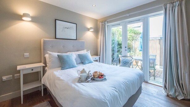 A neatly arranged bedroom with a large bed, bedside tables, and a view of the outdoor patio. - Captain's Quarters, a ground floor apartment in Aldeburgh (Aldeburgh)