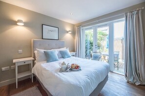 A neatly arranged bedroom with a large bed, bedside tables, and a view of the outdoor patio. - Captain's Quarters, a ground floor apartment in Aldeburgh (Aldeburgh)