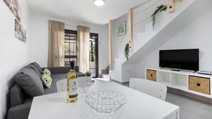 Una sala moderna con una mesa blanca, un sofá gris y un televisor sobre un mueble blanco.