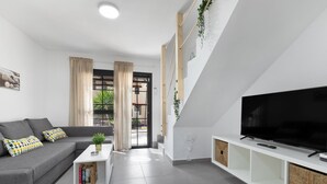 Una sala de estar moderna con un sofá gris, una mesa de centro, un televisor de pantalla plana y una estantería.