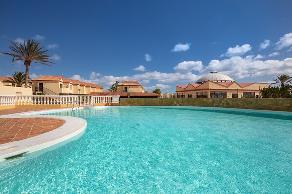 A swimming pool with a tiled deck, a palm tree, and a building with a dome roof.