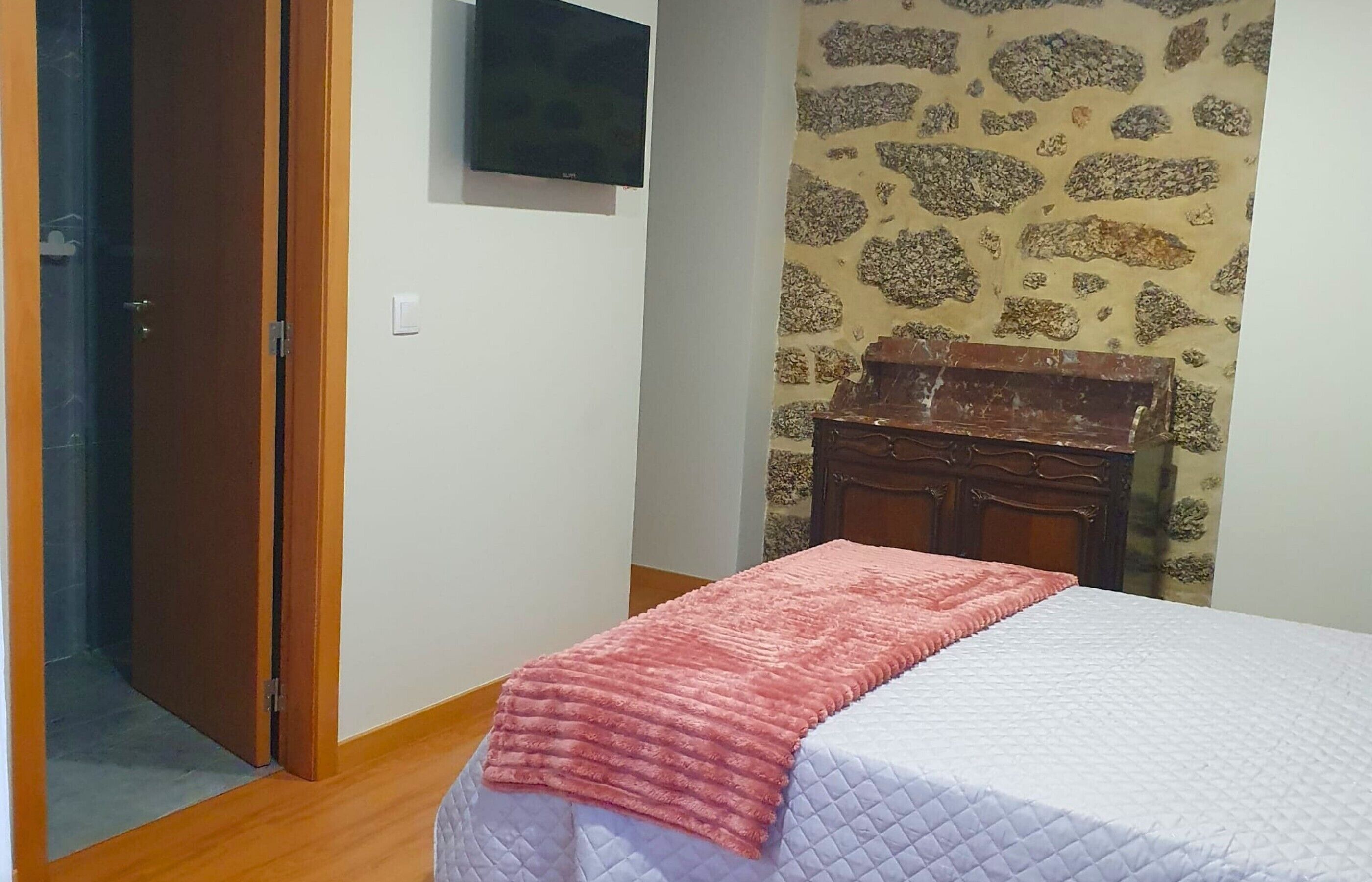 A bedroom with a bed, a wooden dresser, a television, and a stone-patterned wall.