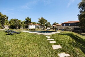 Ein Garten mit Schwimmbad, Liegestühlen und einem Haus mit rotem Ziegeldach.