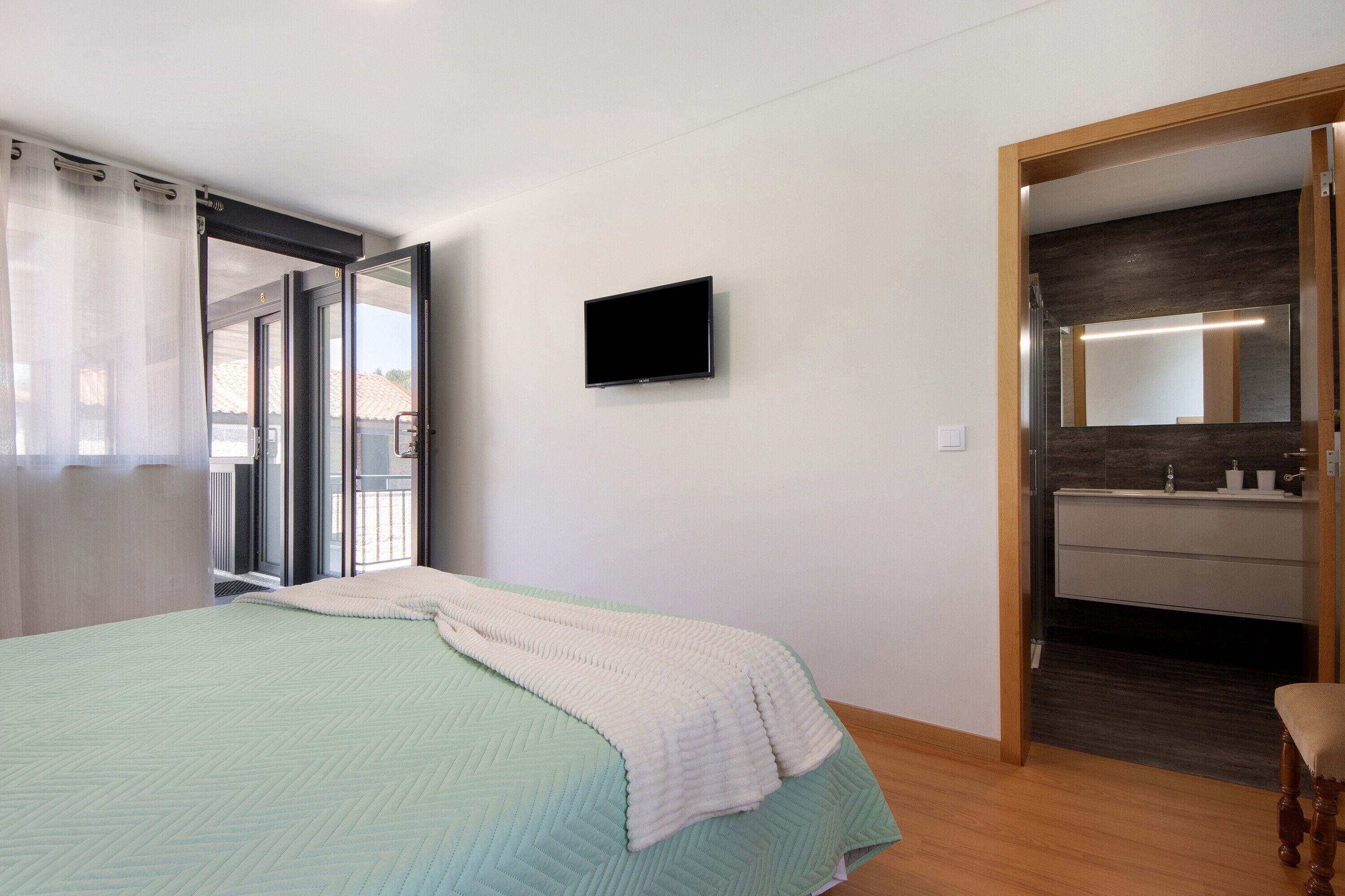 Ein Schlafzimmer mit Bett, Fernseher und einem Badezimmer mit Spiegel sowie einer Schiebetür zu einem Außenbereich.