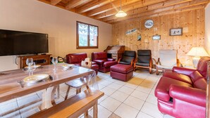 A wooden-paneled room with a dining table set for four, leather sofas, a television, and a clock on the wall.