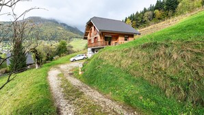 A wooden cabin with a sloped roof, a gravel path leading to it, and a car parked nearby.