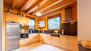 A modern kitchen with wooden cabinets, stainless steel appliances, and large windows.