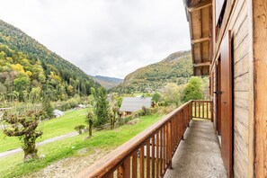 Ein Holzbalkon mit Blick auf ein Tal, ein Haus in der Ferne und ein Baum mit ungewöhnlicher Stammform.