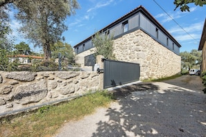 A stone building with a modern extension, a gravel driveway, and a metal gate.
