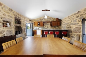 A kitchen with stone walls, wooden cabinets, a dining table with chairs, and a hanging light fixture.