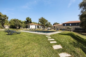 A backyard with a swimming pool, lounge chairs, and a house with a red-tiled roof.