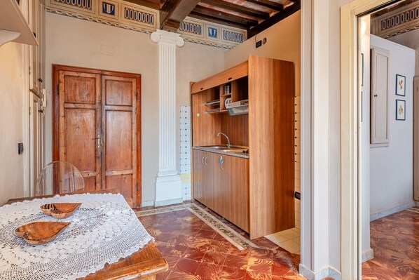 A room with a wooden door, a kitchen area with wooden cabinets, a sink, and a table with a lace tablecloth.