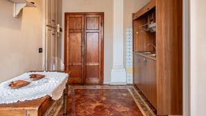 Una habitació amb una porta de fusta, una columna blanca, un armari de fusta i un taulell amb una tovallola de puntes.