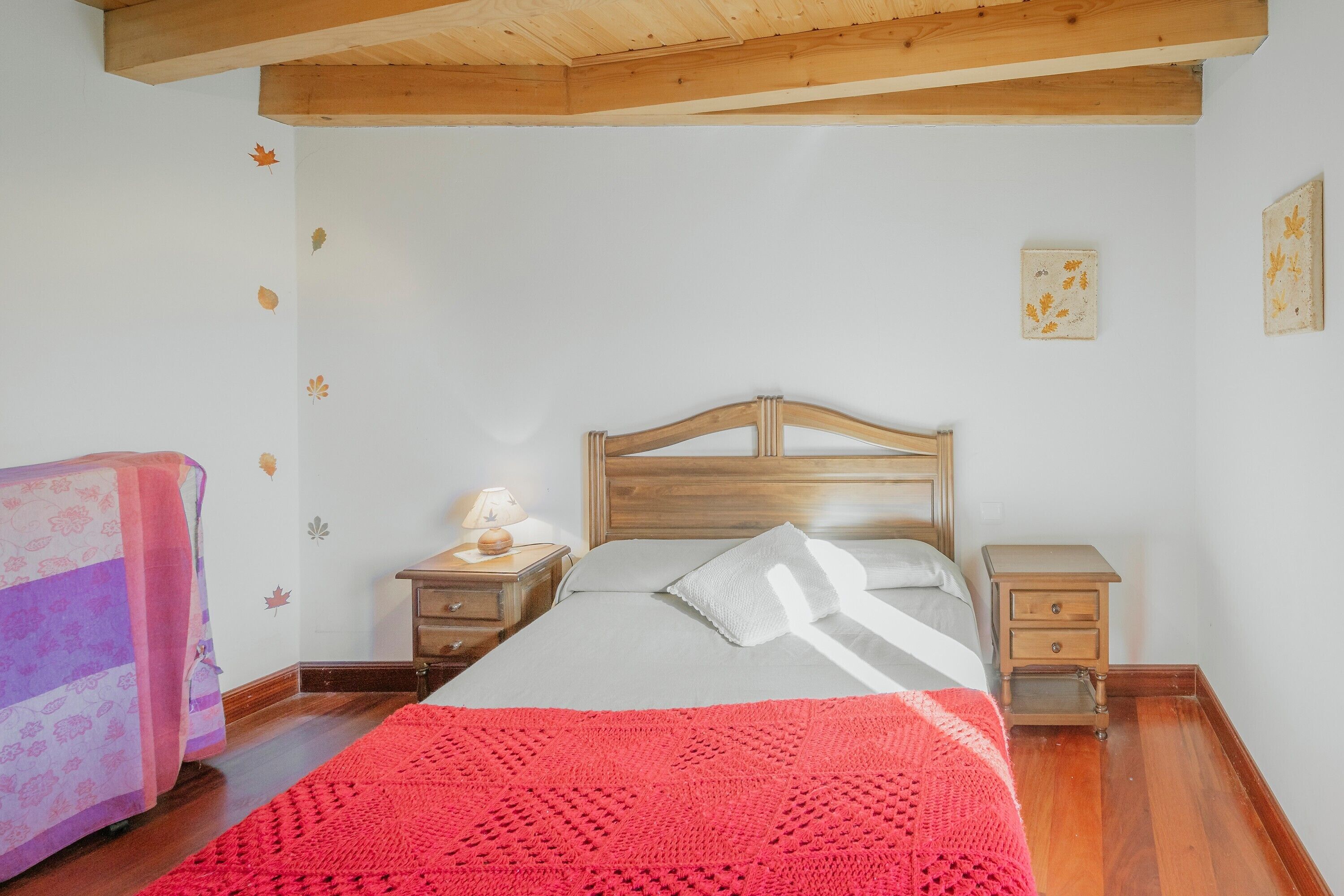 Een slaapkamer met een houten bed, een nachtkastje met een lamp, een dressoir en een rode deken op het bed.