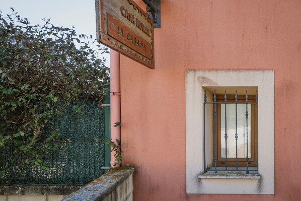A building with a sign reading 'Casa Burro La Cabana,' a window with metal bars, and a green fence with foliage.