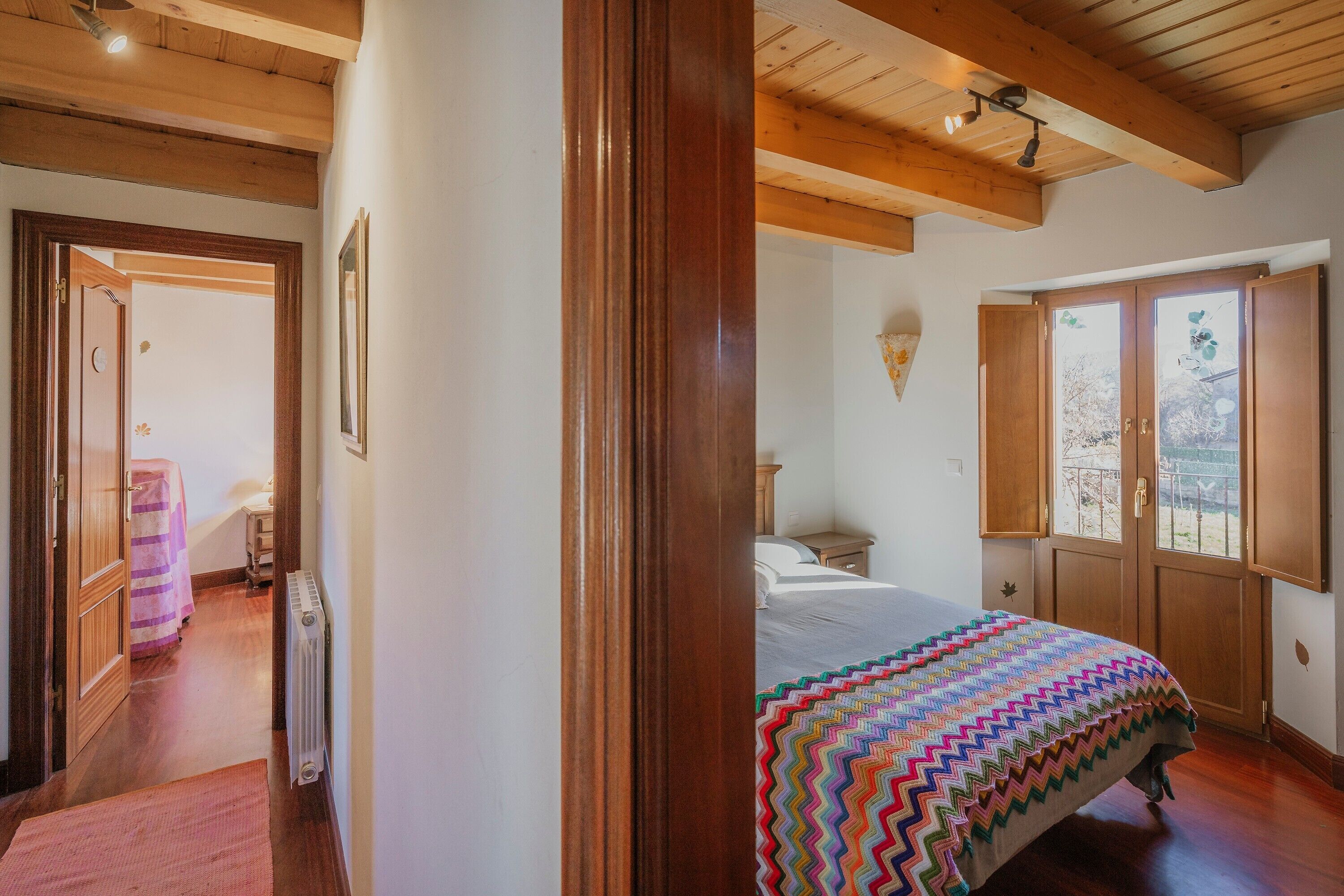 Une chambre à coucher avec un lit, des poutres en bois au plafond, une fenêtre donnant sur un beau paysage et une porte menant à une autre pièce.