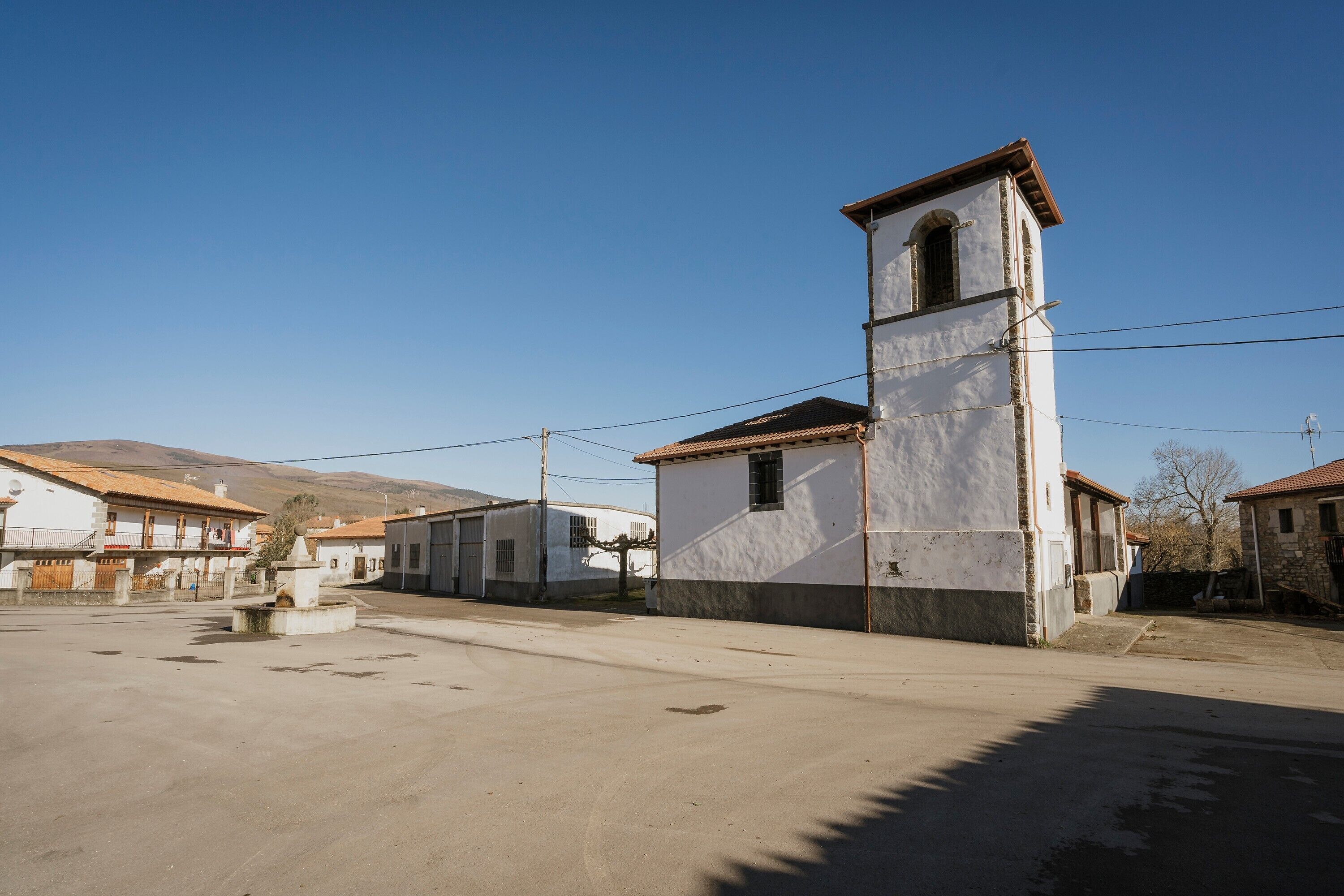 Une rue tranquille, bordée de maisons d’habitation, où se dresse un imposant bâtiment blanc doté d’un clocher.