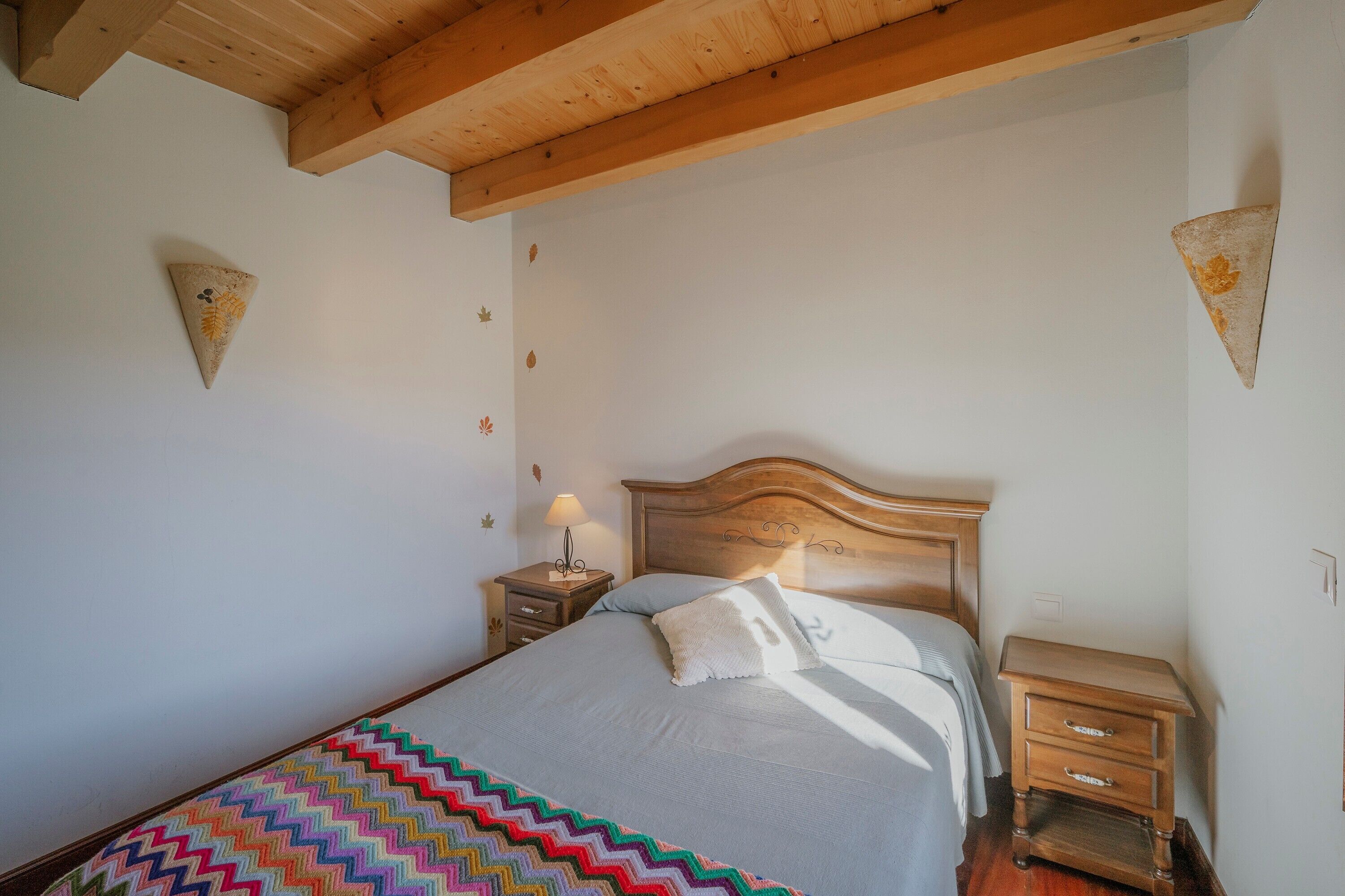 Una camera da letto con testiera in legno, un comodino con lampada e una coperta colorata a motivi a zig-zag.